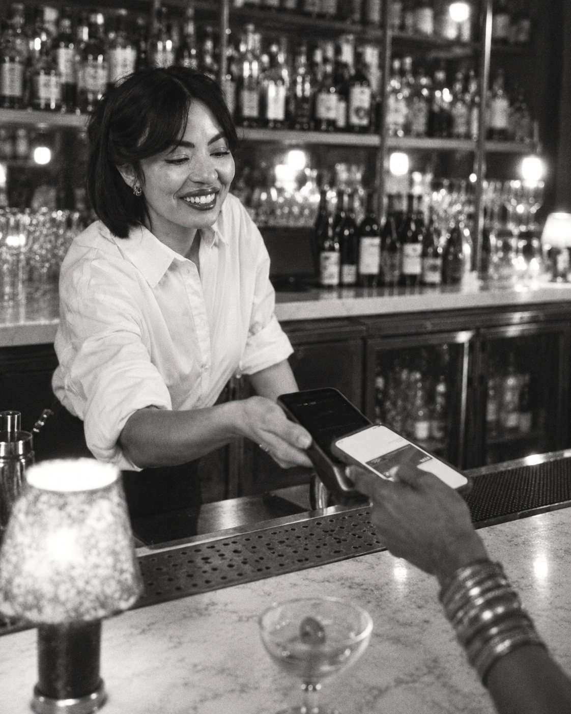 Black-and-white photograph of a customer paying by phone at a bar